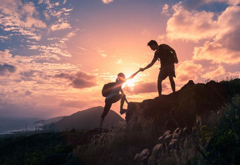 Picture of a hiker helping another hiker up a small cliff (aka: teamwork).