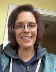 Grace Walker wearing glasses with dyed hair and a blue sweatshirt.