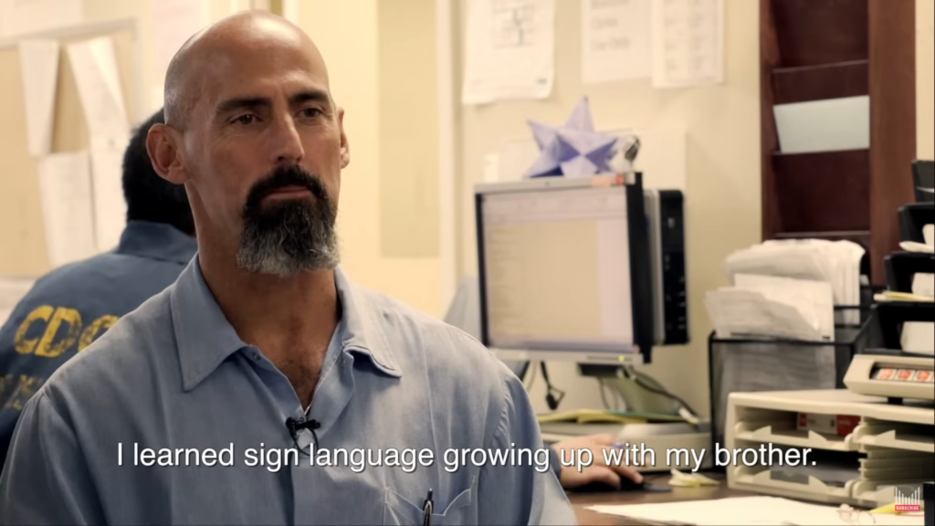 Tommy Wickered wearing a blue shirt, bald head with a blackish goatee talks from prison